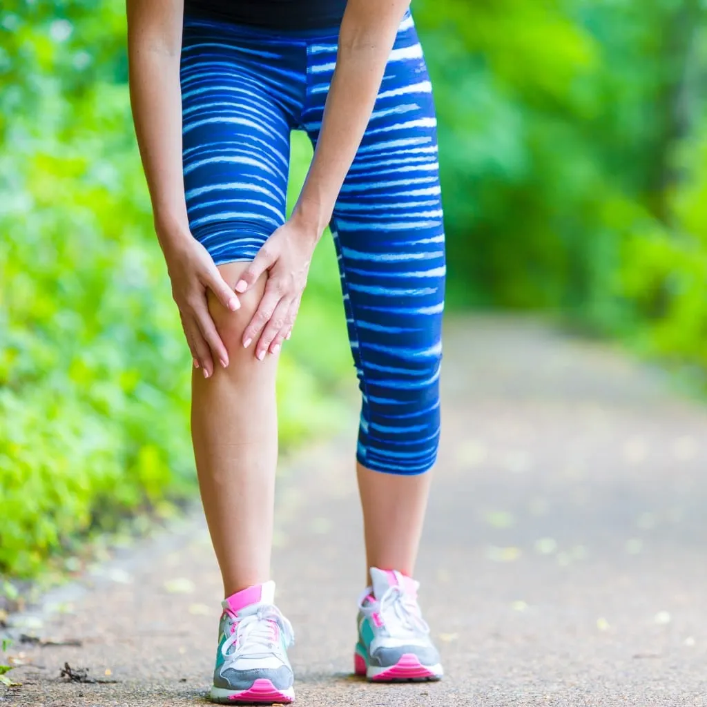 Runner pausing to hold their knee in pain on an outdoor trail